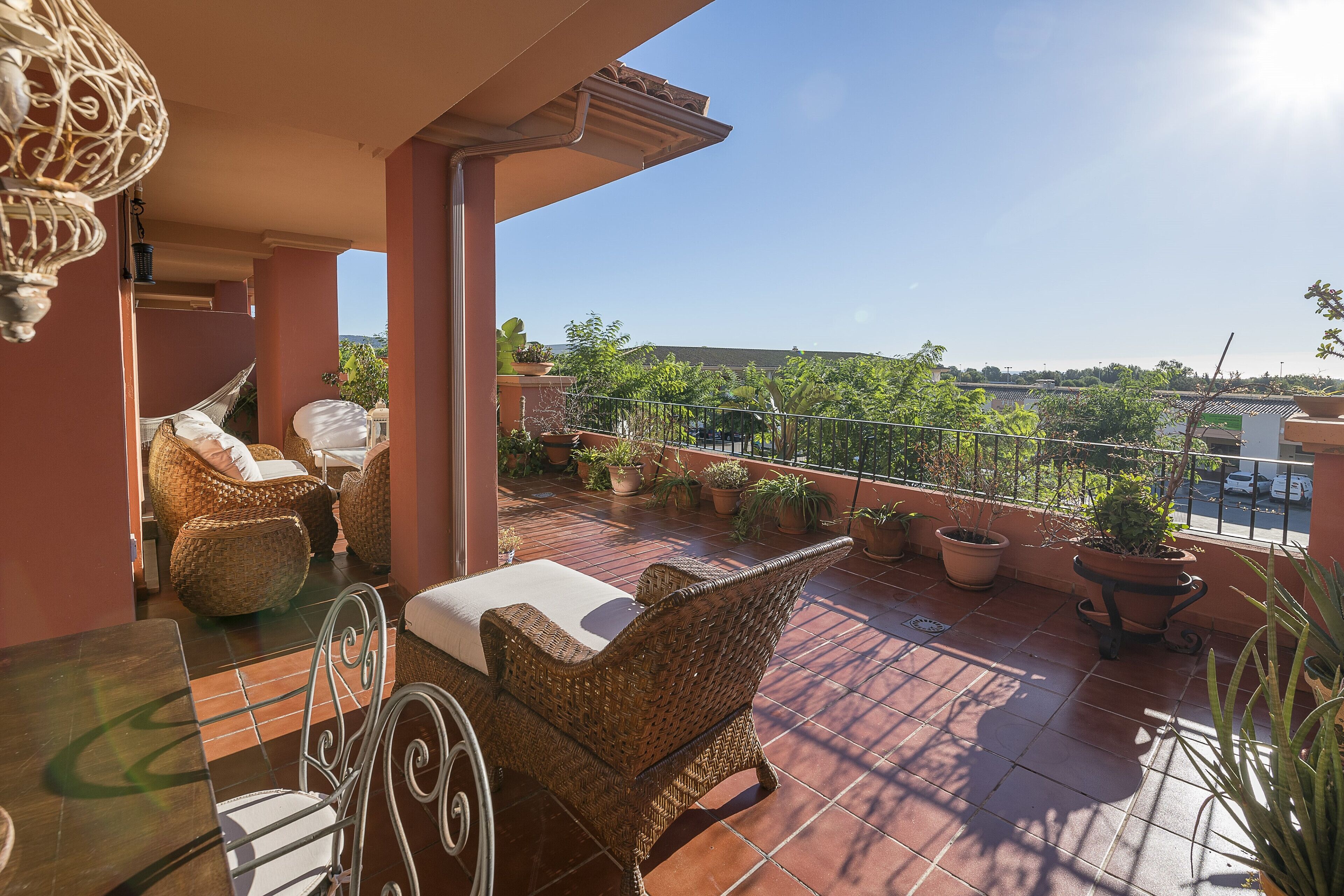 A balcony with wicker furniture, potted plants, and a clear view of the surrounding landscape.