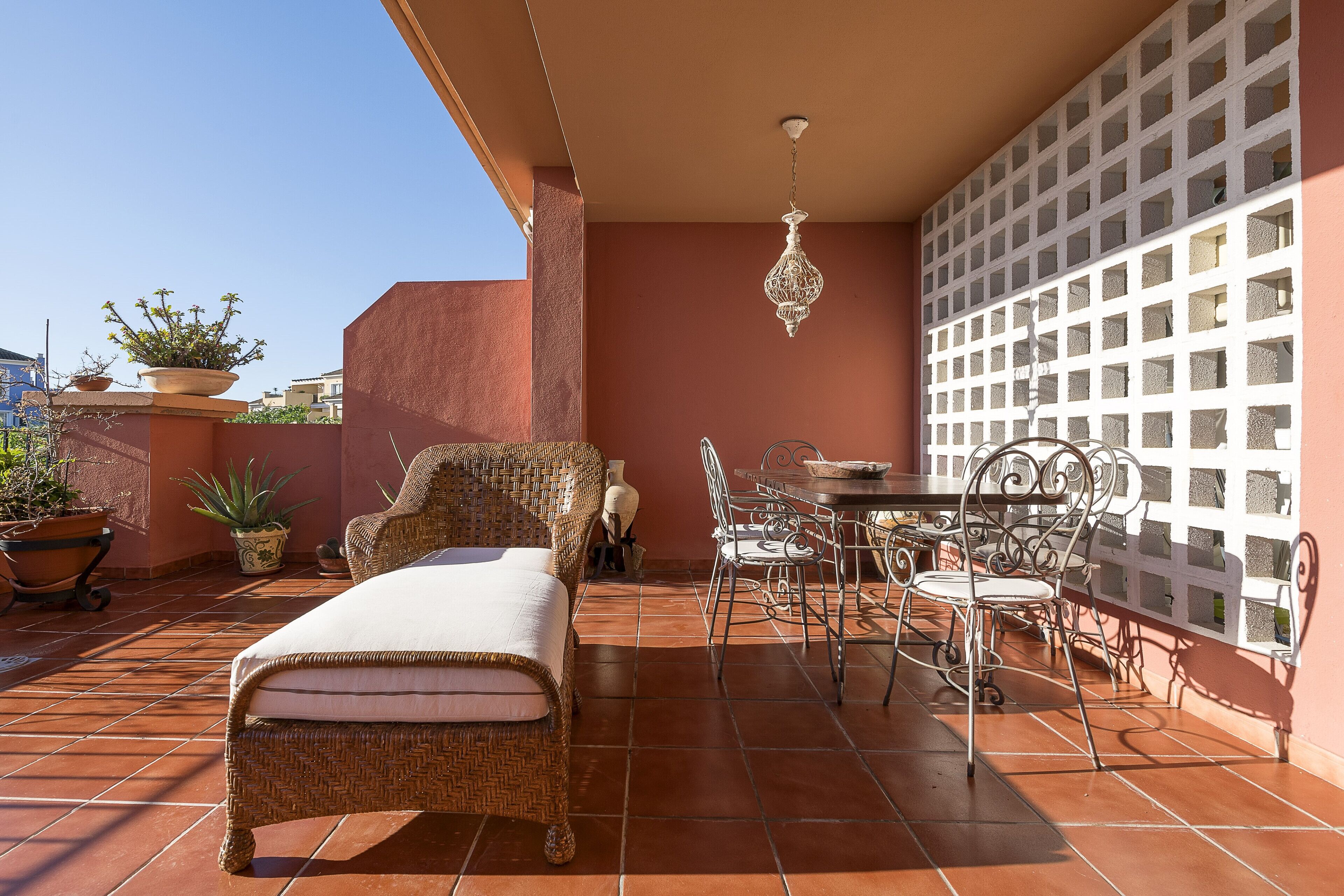 Un patio con un sofá de mimbre, sillas de metal, una mesa de comedor y plantas en macetas.