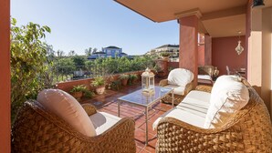 Ein Balkon mit Korbmöbeln, einem Glastisch und Topfpflanzen.
