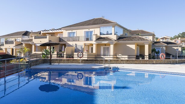 Ein Hotel mit Schwimmbad, mehreren Balkonen und blauem Himmel.