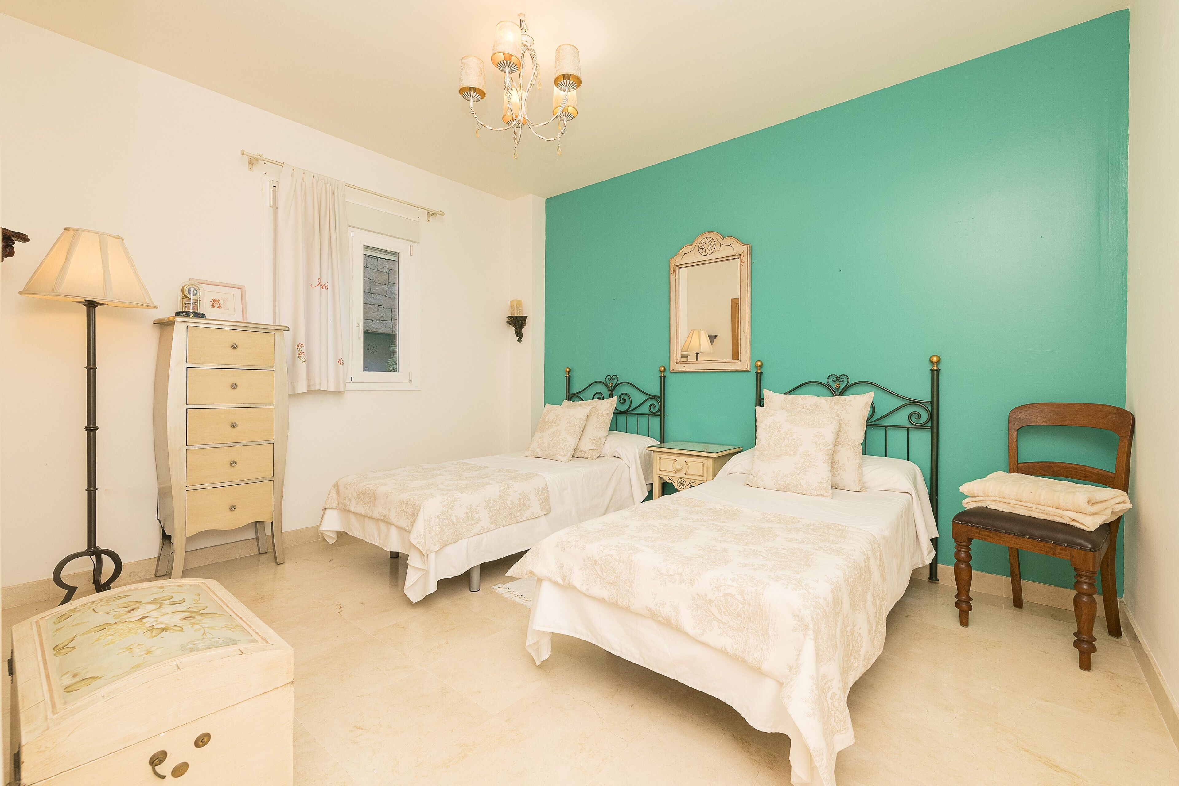 Un dormitorio con dos camas, un aparador, una silla, una lámpara y un espejo.