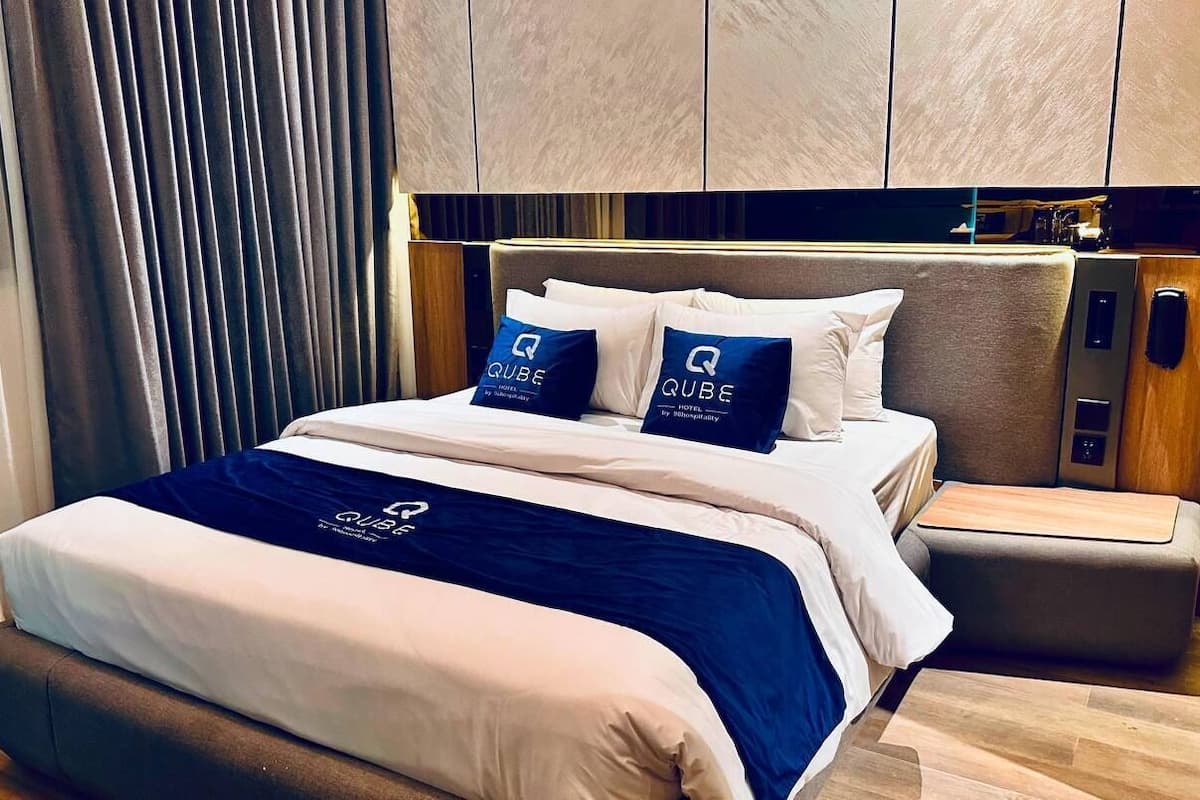 A modern hotel room with a neatly made bed, a bedside table, and a built-in wardrobe.