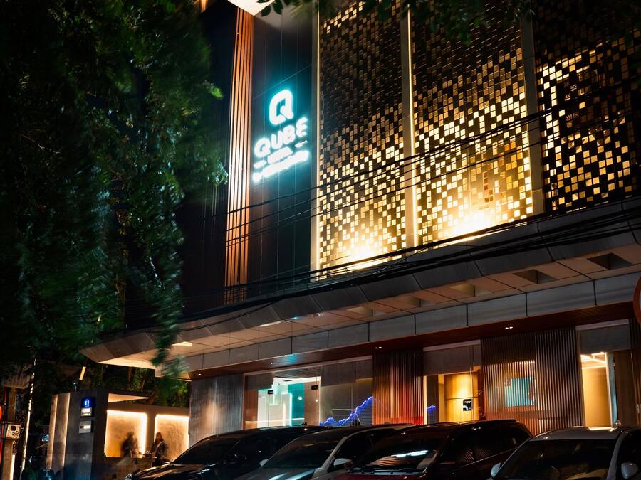 Un hotel con fachada moderna, un llamativo letrero 'QUBE' y varios coches estacionados frente a él.