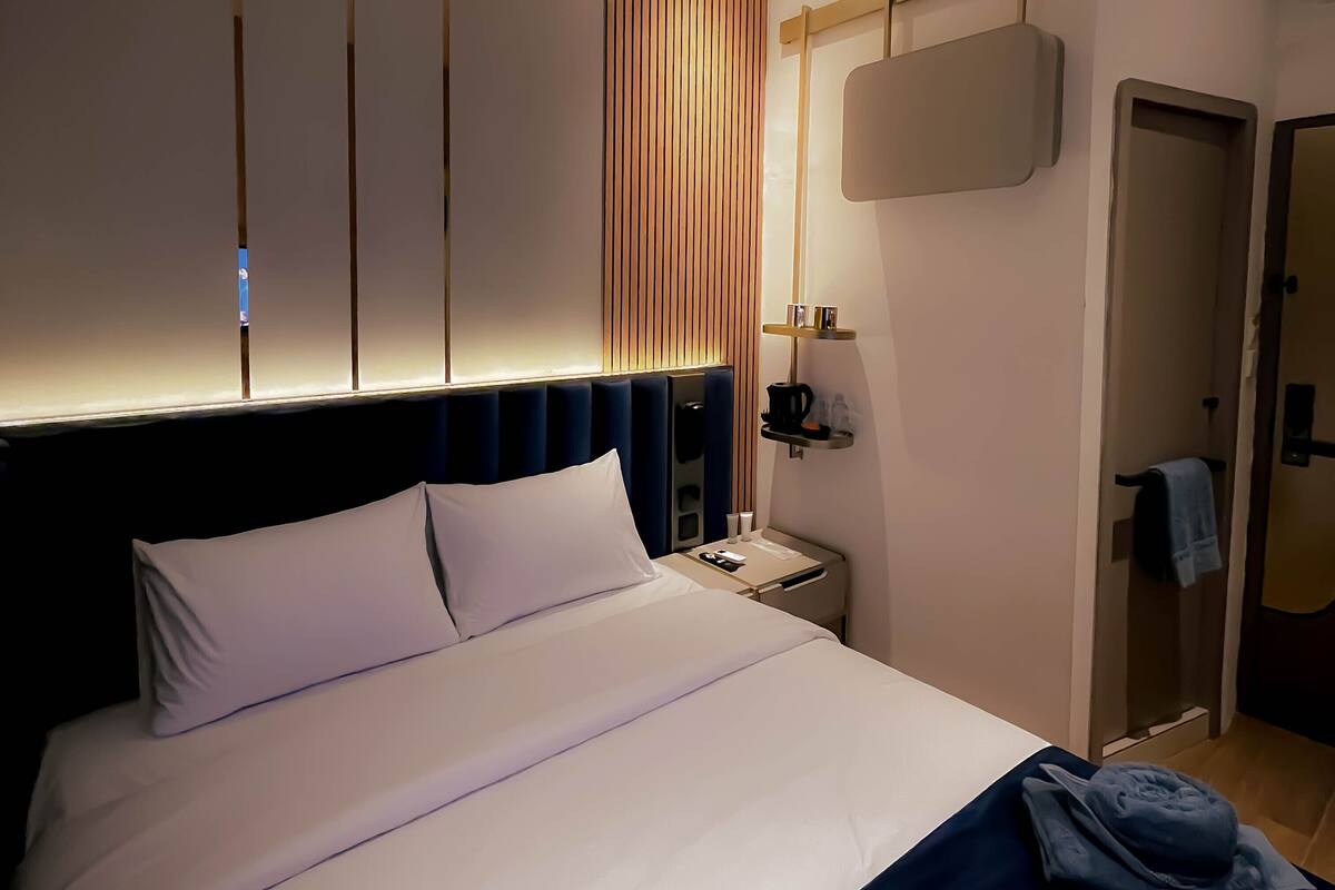 A hotel room with a bed, a nightstand, a wall-mounted TV, and a door.
