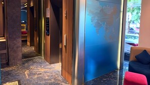 A modern hotel lobby with a marble floor, wooden and metal elevator doors, and a large world map mural on the wall. - Qube Hotel by 98hospitality (Jakarta)
