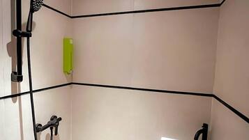 A bathroom with a shower, a sink, and a green towel dispenser.