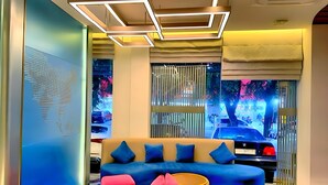 A modern lobby with a blue sofa, colorful cushions, and a large window with a view of the street. - Qube Hotel by 98hospitality (Jakarta)
