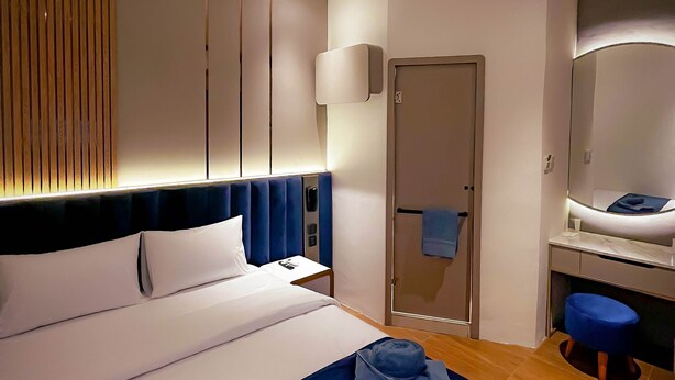 A modern hotel room with a large bed, a bedside table, a bathroom with a mirror, and a wooden floor. - Qube Hotel by 98hospitality (Jakarta)