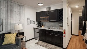 A compact kitchen with dark cabinets, a microwave, and a sink. There is a small dining area with a table and a lamp. - Cozy Condo in Ruidoso ideal for Outdoor Enthusiasts!  (Ruidoso)