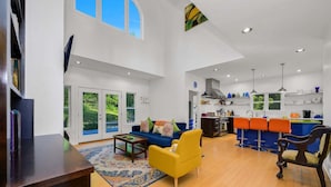 A spacious living area with a sofa, a yellow armchair, a coffee table, and a kitchen in the background. - Sullivan Farm at Helton Creek - Fire Pit - Foosball - Fireplace (Lansing)