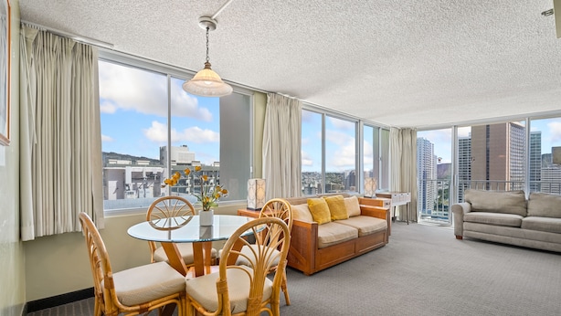 A spacious living room with a dining area, large windows, and a view of the cityscape.
