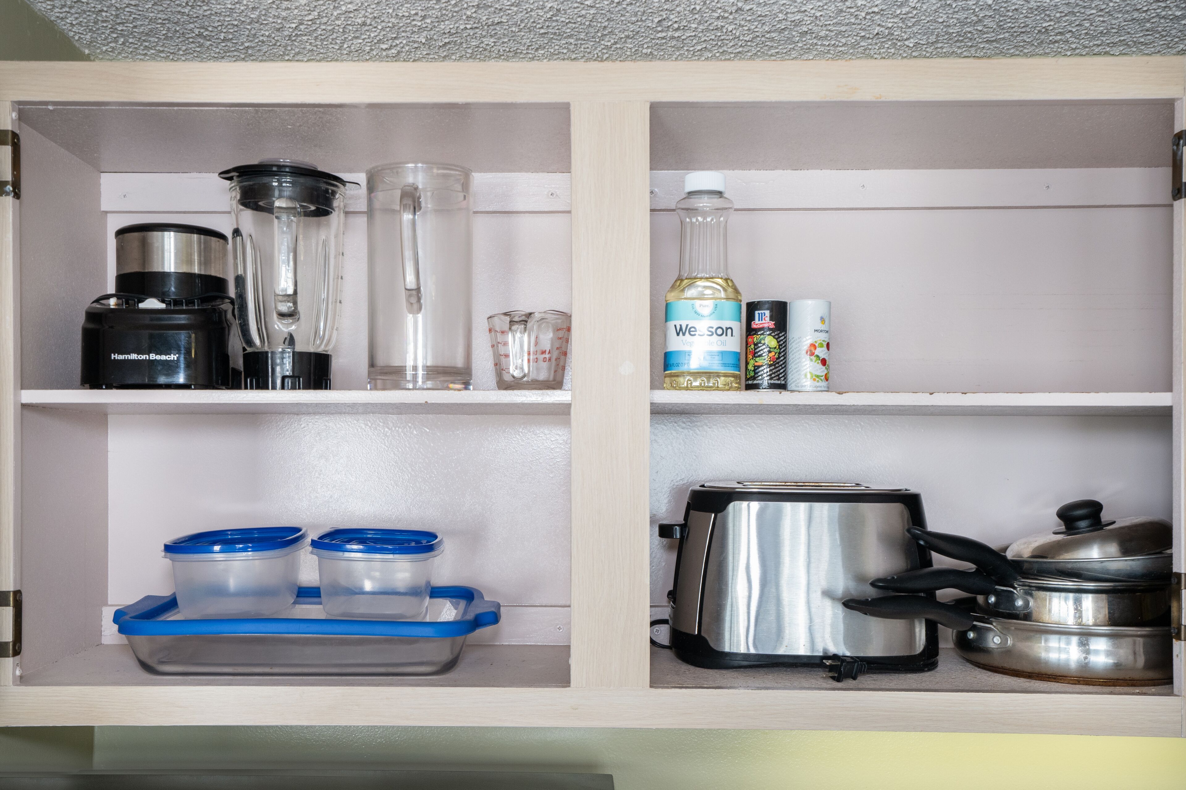 A kitchen cabinet with a blender, measuring cup, Weison dish soap, and a toaster.