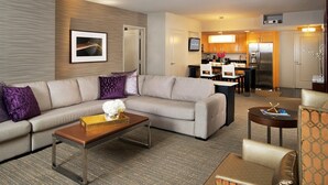 A modern hotel room with a living area featuring a sofa, a coffee table, and a small side table. There is a kitchen area with a refrigerator and a dining table. - Elara Las Vegas Strip - 1 Bedroom Hilton HGVC (Las Vegas)
