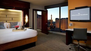 A hotel room with a bed, a desk, a TV, and a view of the Eiffel Tower. - Elara Las Vegas Strip - 1 Bedroom Hilton HGVC (Las Vegas)