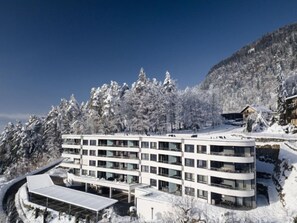 A modern multi-story hotel with a flat roof, surrounded by snow-covered trees and a mountainous backdrop. - Adlerblick alpe maritima Ski & See - 22 by Interhome (Ossiacher See)