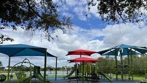Une aire de jeux avec des toboggans, des balançoires et des structures d’escalade, le tout à l’ombre de grands parasols.