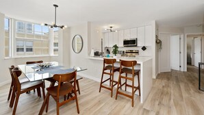 Una cocina moderna con armarios blancos, una isla central y un comedor con sillas de madera y una mesa de vidrio.
