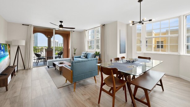 Una sala de estar moderna con una mesa de comedor de vidrio, sillas de madera, un sofá azul y un ventilador de techo.