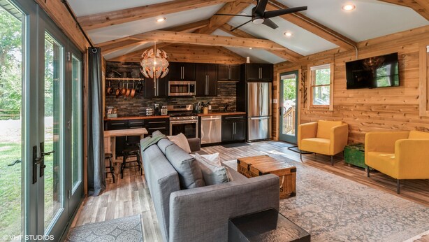 A spacious living area with a gray sofa, yellow armchairs, a wooden coffee table, and a kitchen in the background. -  A cozy, modern cottage has all the amenities and privacy a hotel cannot offer. (Lake Geneva)