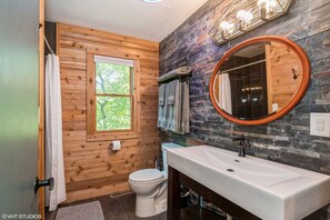 Ein Badezimmer mit Holzwand, Waschbecken in Weiß, rundem Spiegel und Toilette.