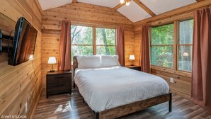 A wooden cabin bedroom with a bed, nightstands, and two windows with curtains. -  A cozy, modern cottage has all the amenities and privacy a hotel cannot offer. (Lake Geneva)