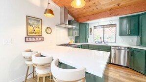 A modern kitchen with a central island, bar stools, green cabinets, and pendant lighting.