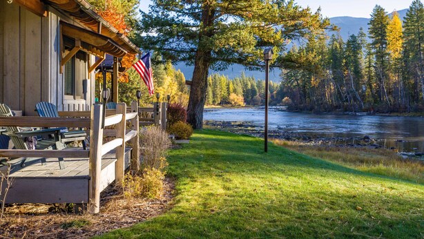 Una cabaña con terraza, un río y un bosque al fondo.