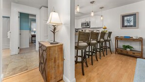 A modern kitchen with white cabinets, a wooden dining table, and bar stools. - Comfort of home, ground floor with in unit laundry (Kihei)