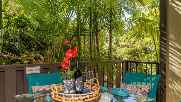 A glass table with a woven centerpiece, a bottle, and a glass. There are two chairs with patterned cushions. - Comfort of home, ground floor with in unit laundry (Kihei)