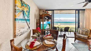 A dining area with a glass table, wooden chairs, and a view of the ocean. - Direct oceanfront views, remodeled condo (Lahaina)