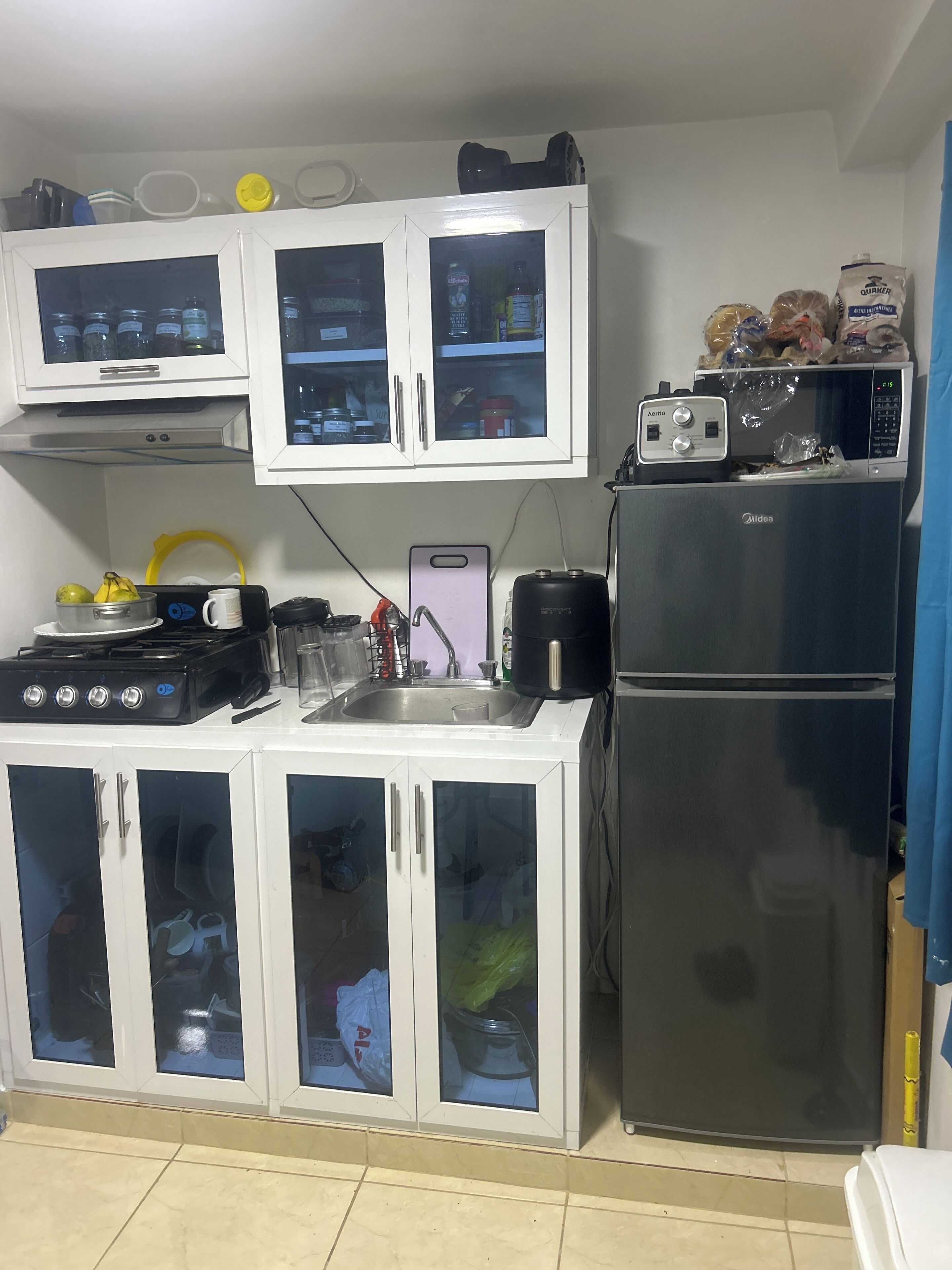 Una cocina compacta con armarios blancos, un refrigerador negro, una estufa y un microondas.