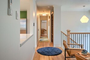 A hallway with a wooden floor, a blue rug, a chair, and a hanging light fixture.