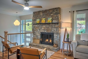 A living room with a stone fireplace, a ceiling fan, a sofa, and a view of the outdoors.