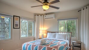 A bedroom with a bed, a ceiling fan, a window, and a bedside table. - Howland House | Asheville | Hot Tub | Pet Friendly | Sleeps 8 (Asheville)