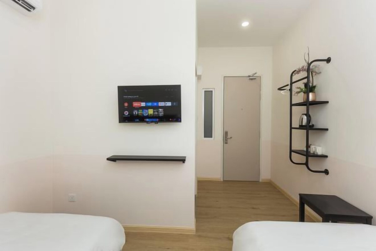 A hotel room with two beds, a mounted TV, a shelf, and a small table.