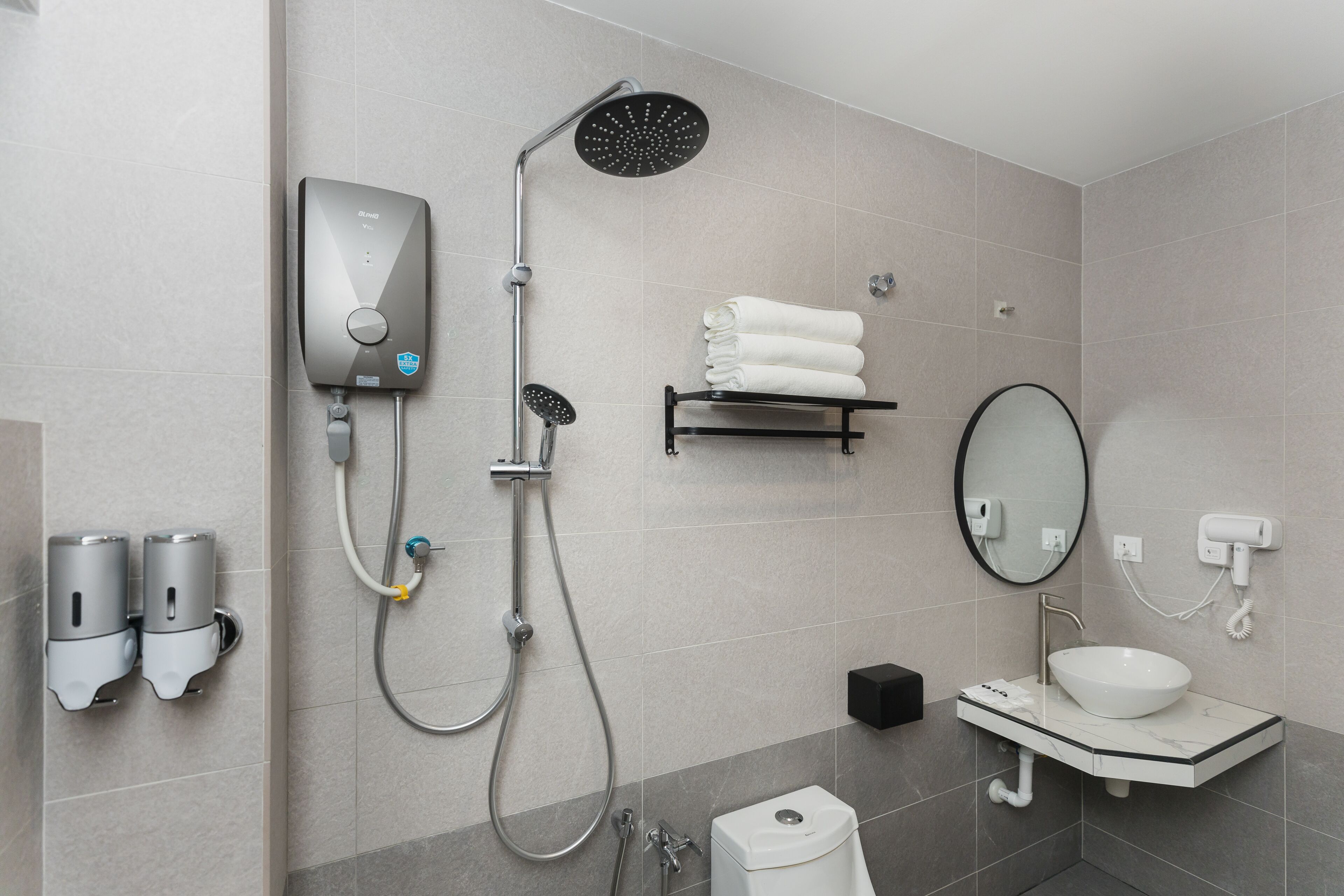 Un baño moderno con ducha integrada, dispensador de jabón de pared, toallero, lavabo con espejo e inodoro.