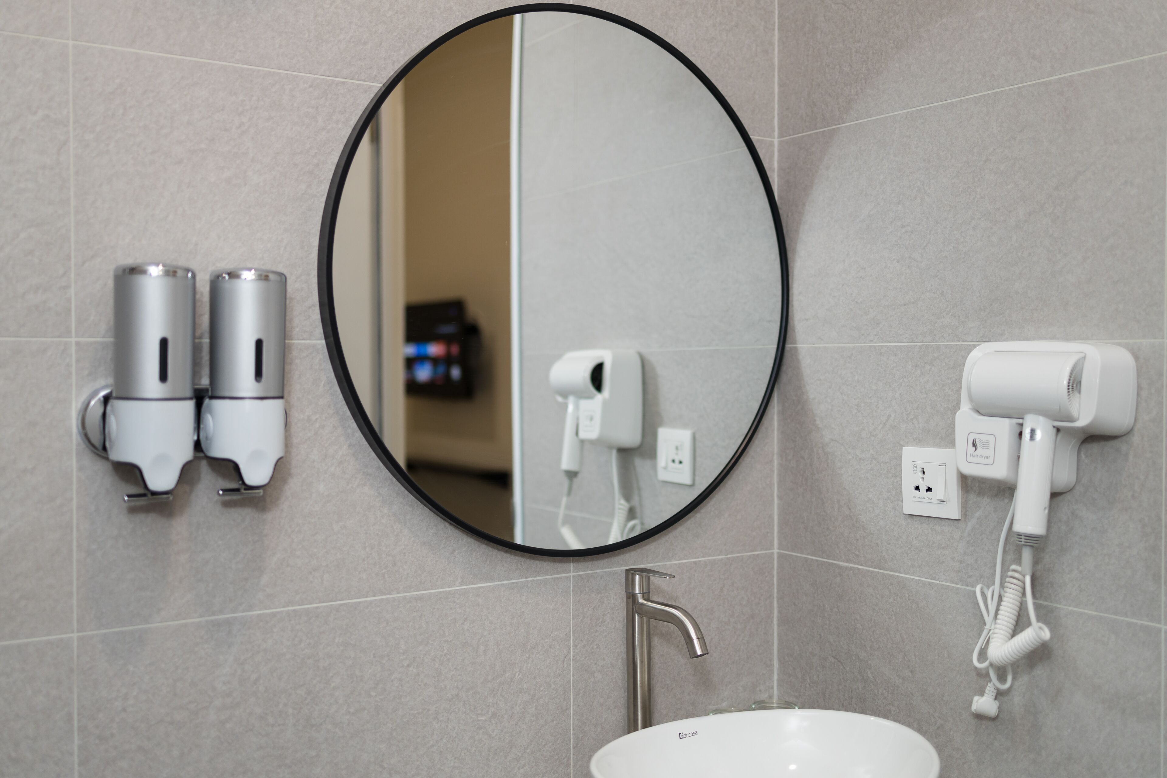 A bathroom with a round mirror, two hand dryers, a sink, and a faucet.