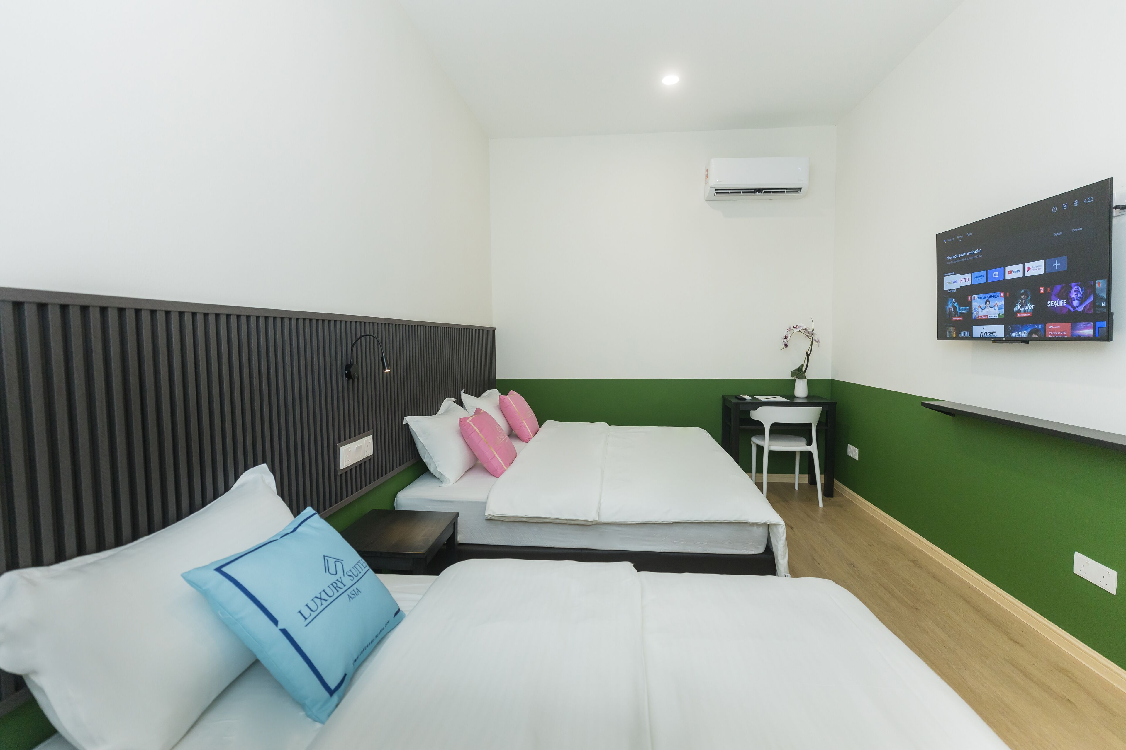 Una habitación de hotel con dos camas, un televisor montado en la pared, una mesita y una silla.