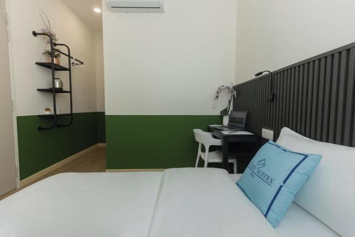 A hotel room with a bed, a desk with a computer, a chair, and a shelf with a plant.