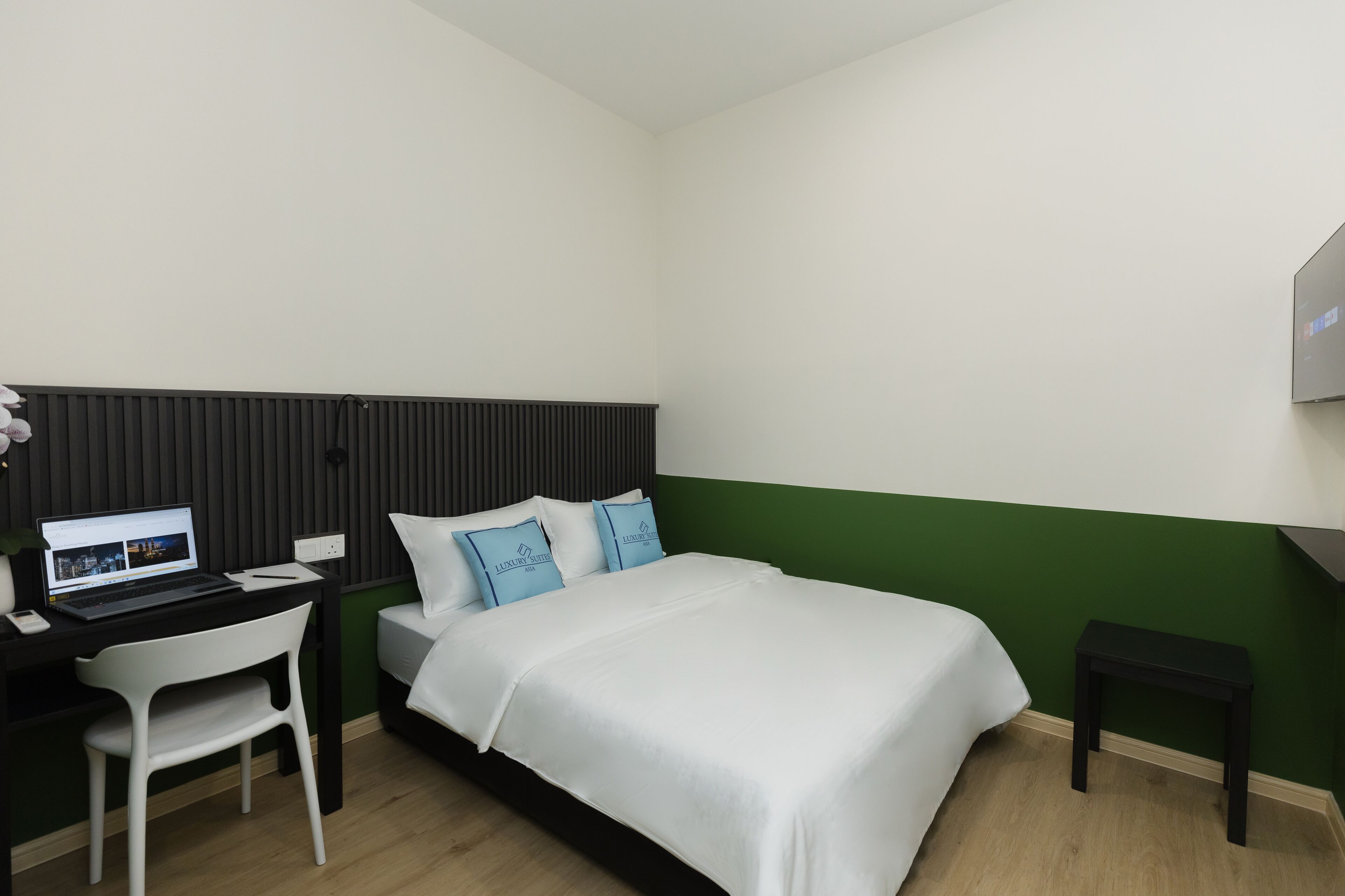 A hotel room with a bed, a desk with a laptop, a chair, and a small table.