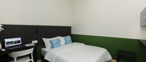 Hotellihuone, jossa on sänky, työpöytä kannettavalla tietokoneella, tuoli ja pieni pöytä.