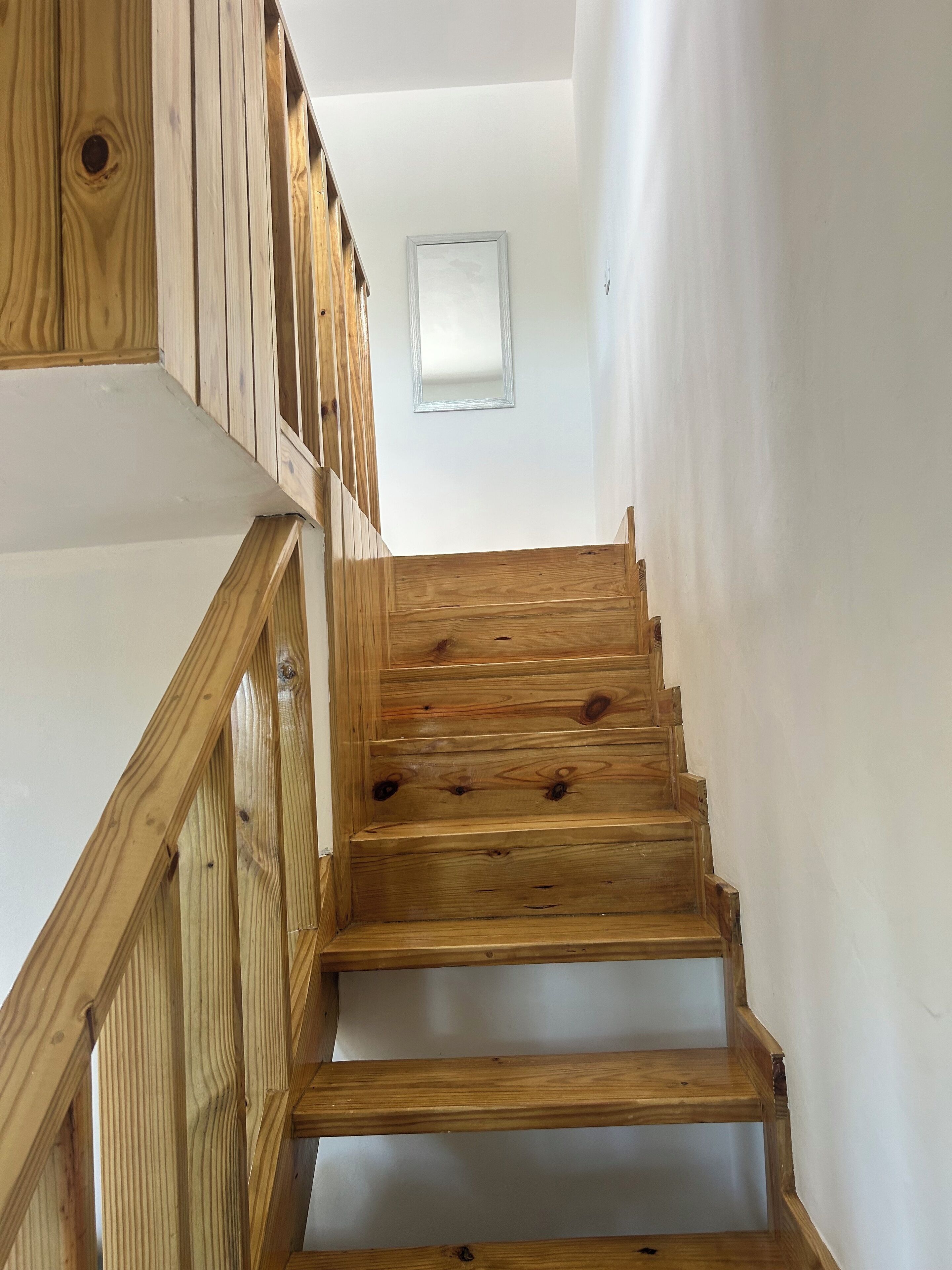 Una escalera de madera con paredes blancas y un ventanal pequeño en la parte superior.