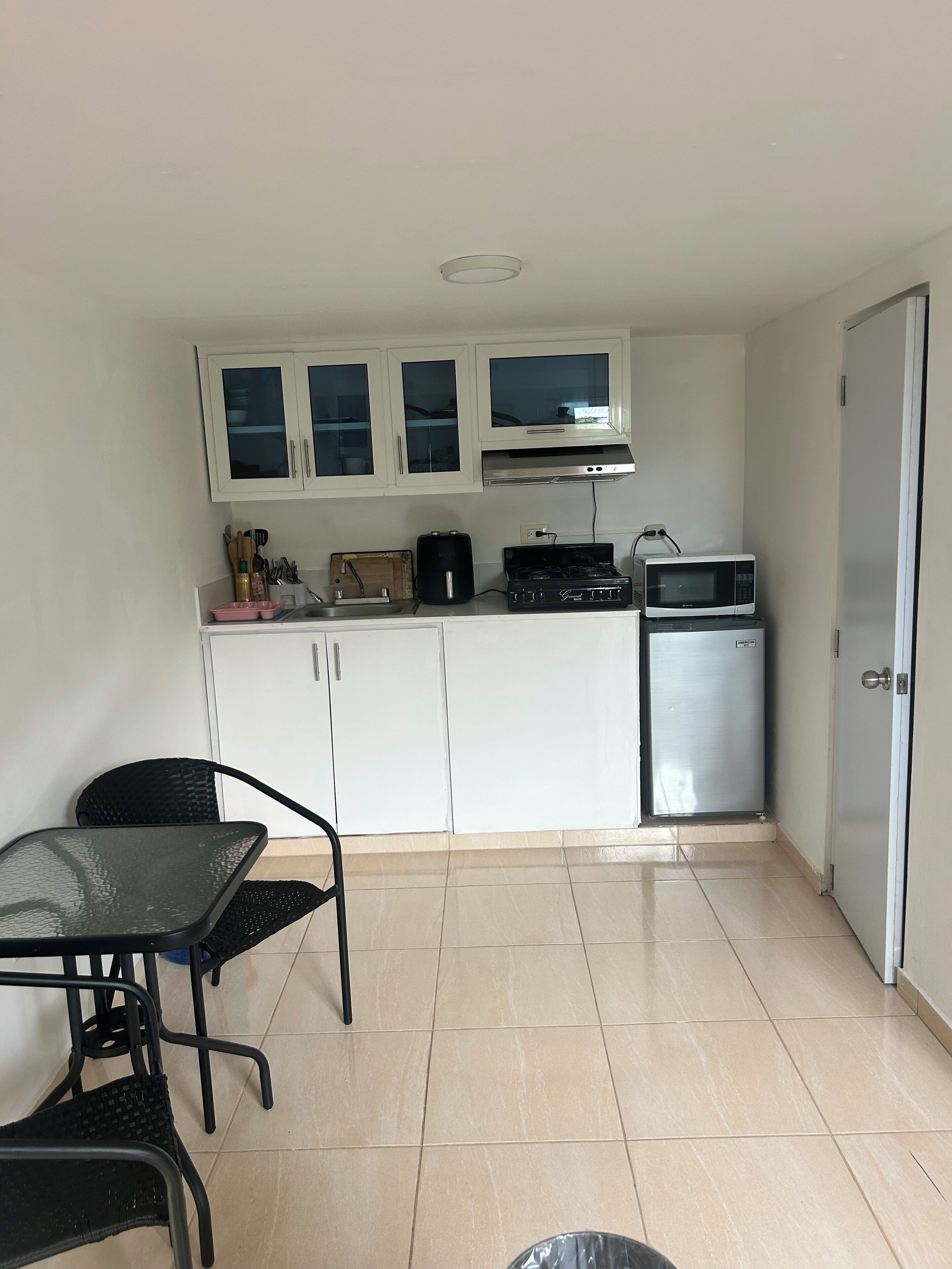A compact kitchen with white cabinets, a microwave, a small refrigerator, and a dining area with a table and chairs.
