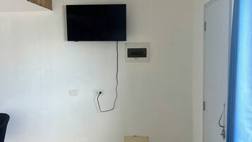 Habitación con una televisión de pantalla plana montada en la pared, un termostato y una puerta con manija.