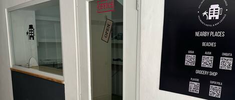 A hotel reception area with a glass door marked "OPEN" and a sign listing nearby places like beaches and a grocery shop.
