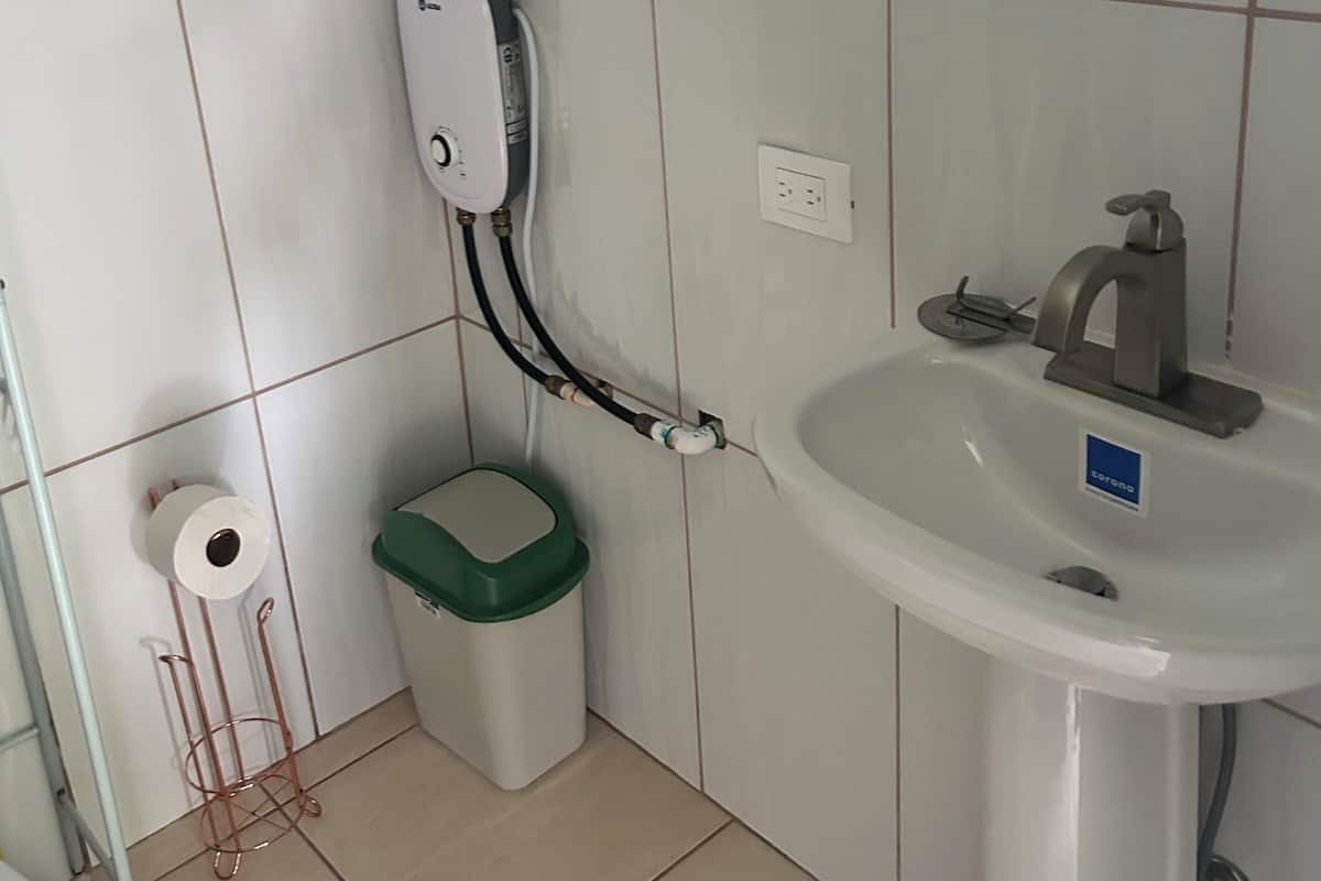 Ein Badezimmer mit einem weißen Waschbecken, einer grünen Mülltonne, einer Toilette und einem Wandtrockner.