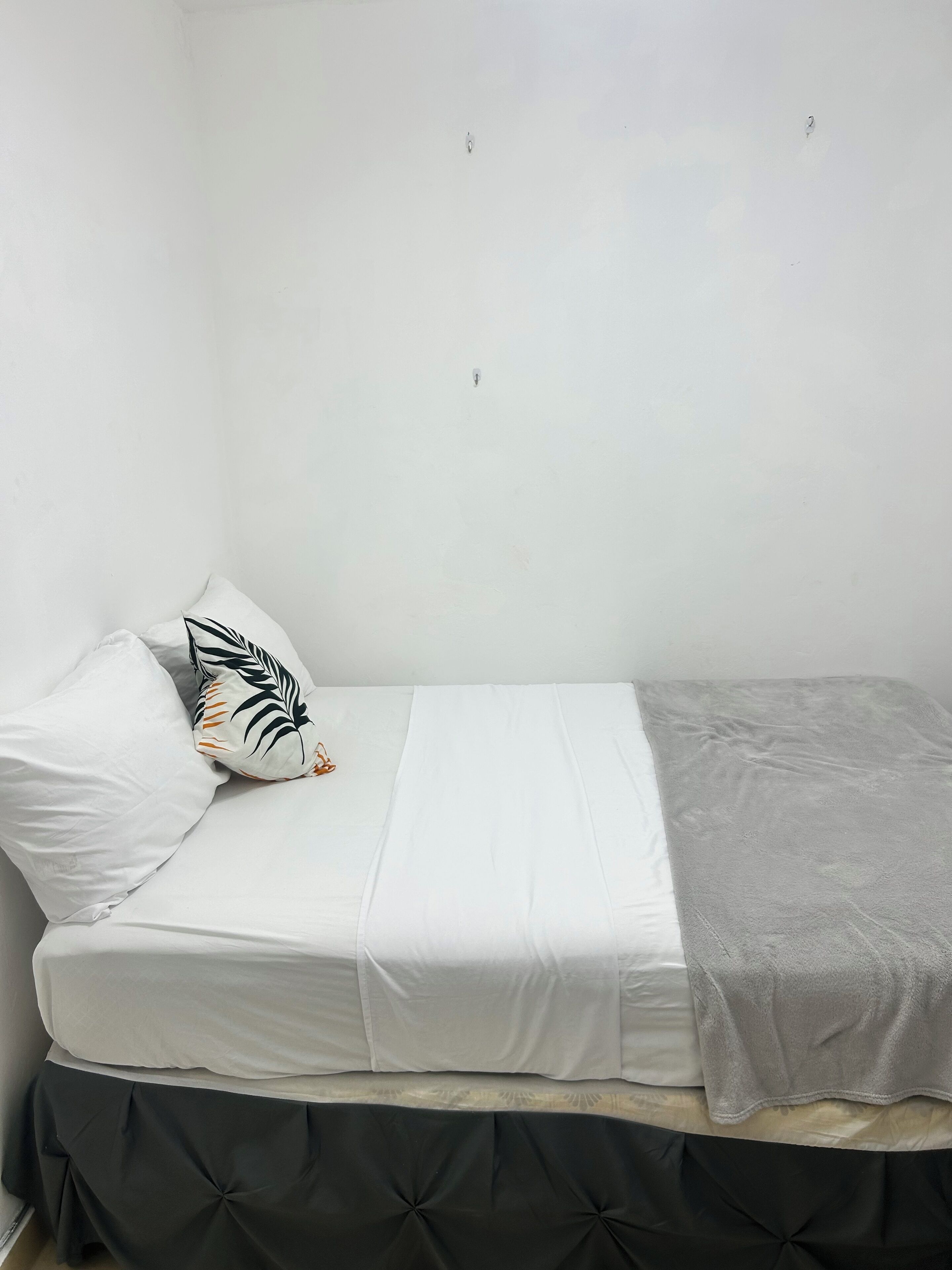 A small, single-bed room with a white bedspread, a grey blanket, and a black upholstered headboard.