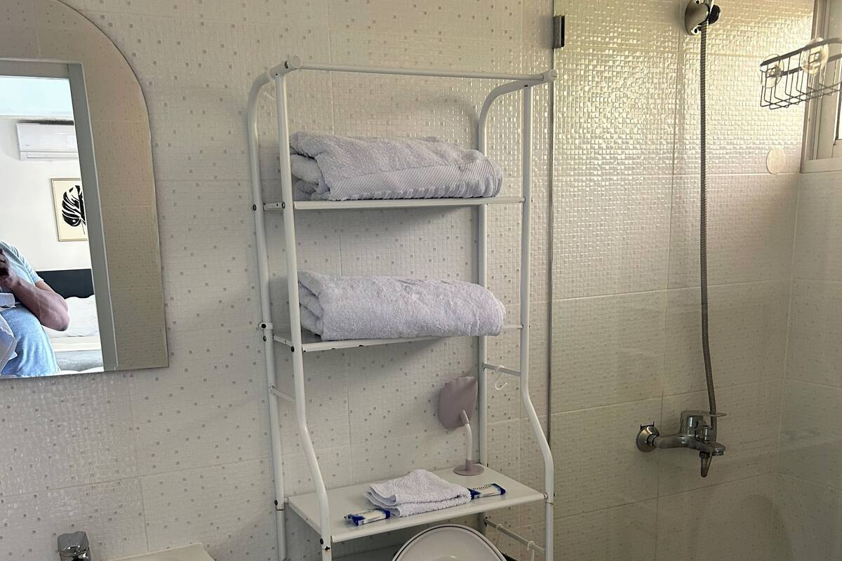 Ein Badezimmer mit Toilette, Waschbecken und Dusche. Ein Handtuchhalter mit Handtüchern und eine Seifenspender sind vorhanden.