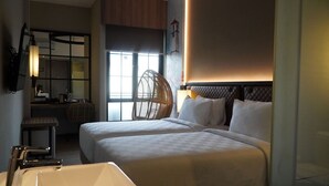 A hotel room with two beds, a large window, a sitting area with a chair, a small table, and a bathroom with a sink and mirror. - Posto Dormire Benhil (Jakarta)