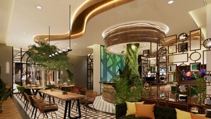 A modern hotel lobby with a curved ceiling, a central seating area with tables and chairs, a large green plant, and a wall with mirrors and framed pictures. - Posto Dormire Benhil (Jakarta)